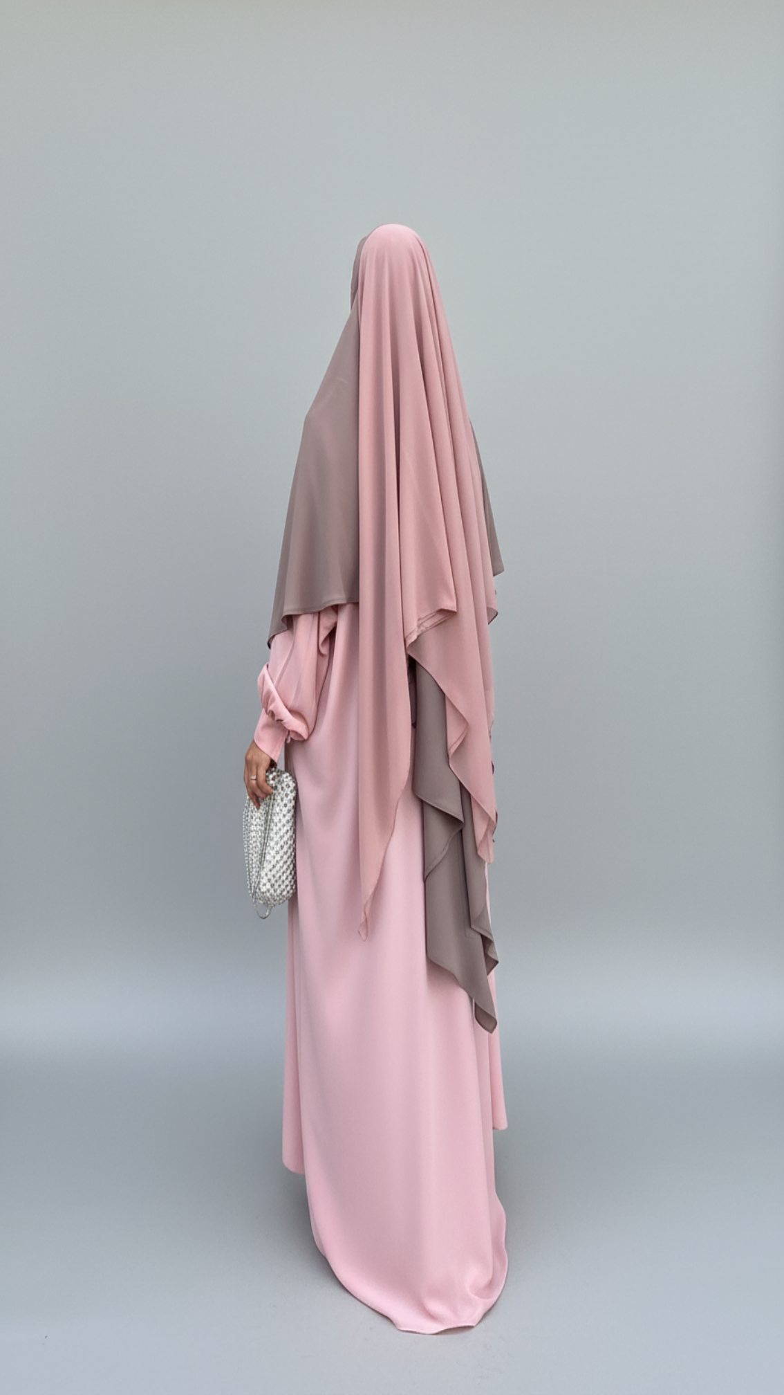 Person wearing a pink and gray hijab and dress on a gray background